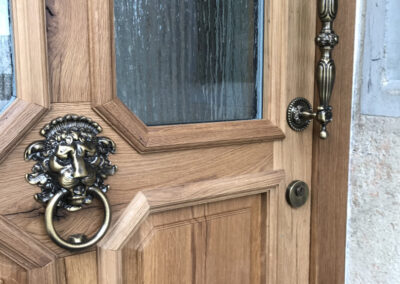 Detailaufnahme einer Türe aus massivem Holz mit Löwenkopf-Türklopfer und kunstvollem Griff. Schreinerarbeit in höchster Qualität.