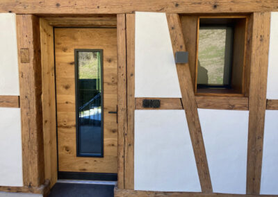 Moderne Massivholztüre mit schmalem Glaseinsatz, perfekt kombiniert mit rustikalem Fachwerk. Schreinerarbeit aus massivem Holz.